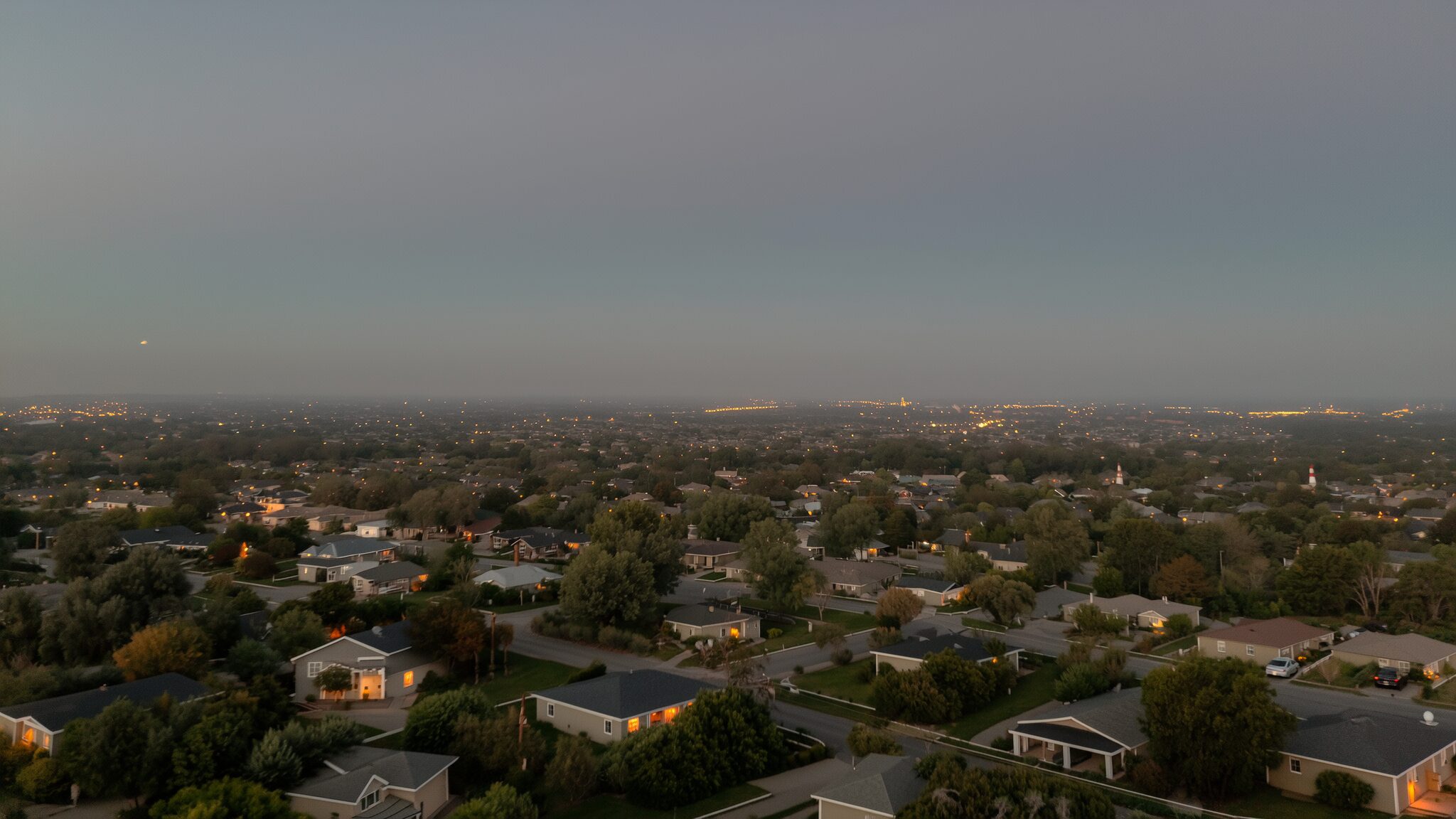 A neighborhood at dusk with warm window lights stretching to the horizon
